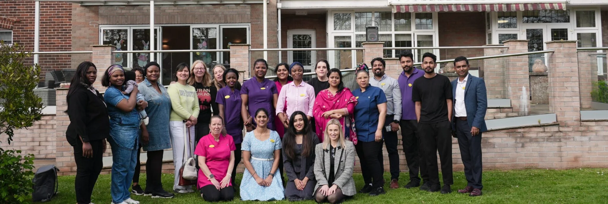 Group photo of diverse staff in front of a brick building, showing teamwork and community spirit.